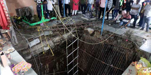 People stand around a structure built over an old temple well that collapsed on March 30, 2023, in Indore, India. At least eight people died when the well collapsed.