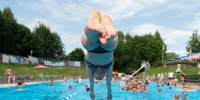 A swimmer jumps from a starting block into the water pool of an outdoor swimming pool, North Rhine-Westphalia, Bielefeld, Germany, Aug. 4, 2022.