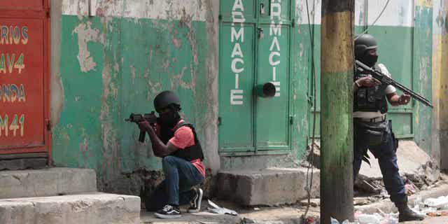 Police officers take cover during an anti-gang operation in Haiti