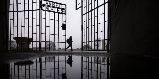 A person walks behind the gate of the Sachsenhausen Nazi death camp with the phrase 'Arbeit macht frei' (work sets you free) in Oranienburg, about 30 kilometers (18 miles) north of Berlin, Germany, Tuesday, Jan. 25, 2022. 