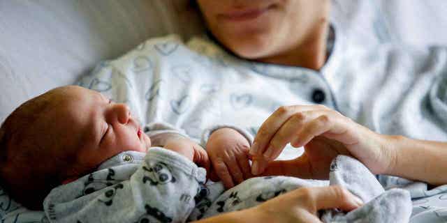 A newborn baby rests in his mom's arms, inside a room of the Santo Spirito Hospital in Rome, Italy, on Nov. 14, 2022. The birth rate in Italy hit a record low in 2022.