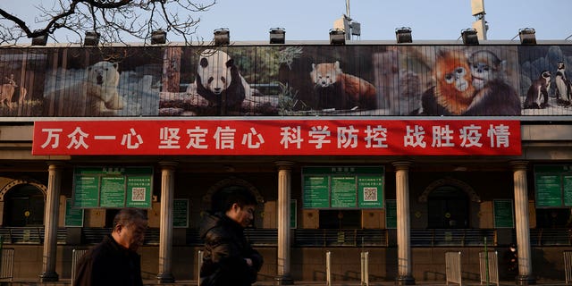 Men walk past a banner hung at the Beijing Zoo on Feb. 10, 2020. The banner reads "Stay focused and united, have faith and confidence, with scientific prevention and control, we can beat the epidemic." China has decided not to participated in a UN wildlife survey aimed at preventing future pandemics due to zoonotic transmission. 
