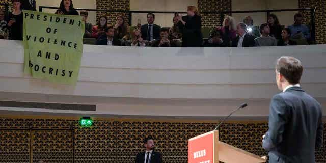 French President Emmanuel Macron looks at demonstrators unfolding a banner reading "President of Violence and Hypocrisy" during a speech in The Hague, Netherlands, on April 11, 2023. 