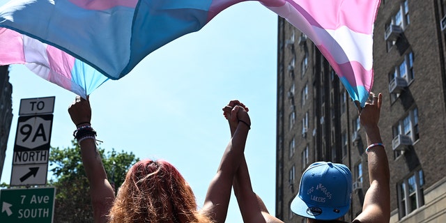 Two trans people hold hands while marching under a trans pride flag in the New York City Pride Parade on June 26, 2022, in New York City.