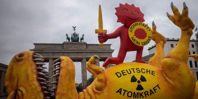 A mock-up dinosaur lies in front of the Brandenburg Gate during a rally marking the nuclear shutdown in Germany in Berlin, Germany, Saturday, April 15, 2023.