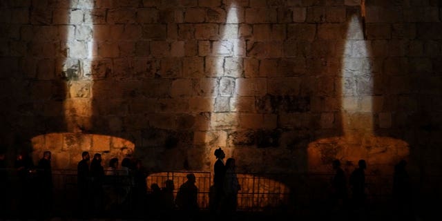 People walk by an image of memorial candles, projected on the walls of Jerusalem's Old City on the eve of annual Holocaust Remembrance Day on April 17, 2023.