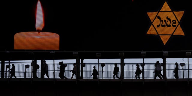 People walk along a bridge under a billboard showing a yellow Star of David that reads Jew in German during the annual Holocaust Remembrance Day in Ramat Gan, Israel, on April 18, 2023. Israel’s Day of Remembrance commemorates the six million Jewish victims who were killed by Nazi Germany.