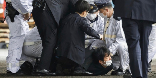 A man believed to be a suspect, center on the ground, is caught by police after he allegedly threw "the suspicious object," as Japanese Prime Minister Fumio Kishida visited Saikazaki port for an election campaign event in Wakayama, western Japan Saturday, April 15, 2023. 