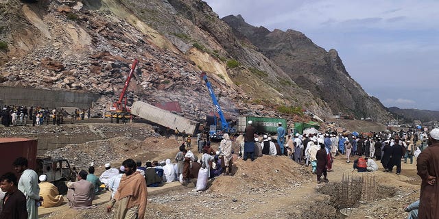 Residents gather as authorities use heavy machines to clear the rubble following a landslide that struck a highway near Torkham, Pakistan, on April 18, 2023. 