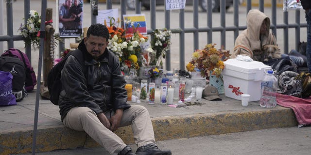 A Venezuelan migrant sits on the sidewalk where an altar was created with candles and photos outside the Mexican immigration detention center in Ciudad Juarez, Mexico, on March 30, 2023.