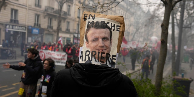 A demonstrator has a poster mocking French President Emmanuel Macron over his head during a demonstration March 28, 2023, in Paris.