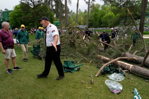A security guard moves people away from trees that blew over on the 17th hole of the Augusta National Golf Club on Friday. No injuries were reported.