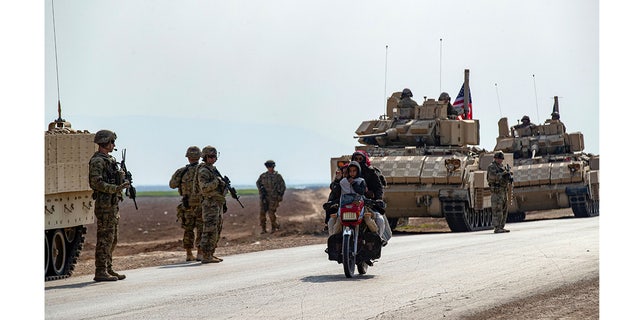 FILE: Members of a family ride a motorcycle as a US military convoy patrols the area near the town of Tal Hamis, southeast of the city of Qameshli in Syria's northeastern Hasakeh governorate, on January 26, 2023. 