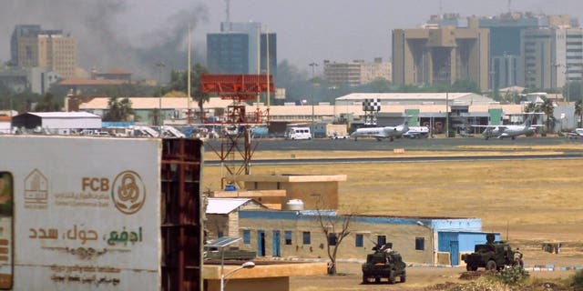 Military vehicles can be seen as smoke bellows above buildings in the vicinity of the Khartoum airport on April 15, 2023, amid clashes in the city.