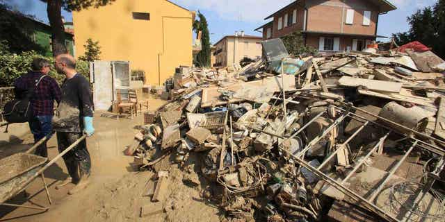 Volunteers clear mud as household goods are piled on the side of a street in Faenza, Italy, 