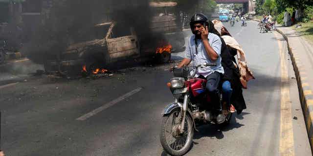A motorcyclist drives past a burning vehicle