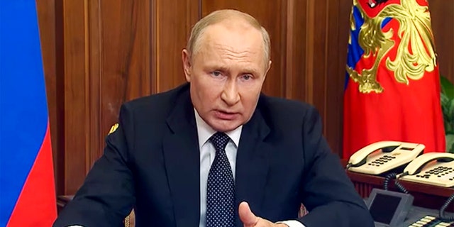 Russian President Vladimir Putin delivers address to the nation while wearing a dark suit and sitting at a desk
