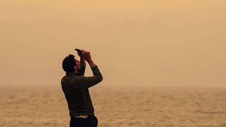 A man takes a photo of the sky.