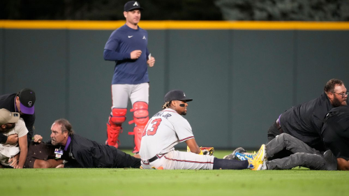 Atlanta Braves right fielder Ronald Acuna Jr., bottom center, sits on the turf as field guards wrestle two fans who approached him in the outfield in the Braves' game against the Colorado Rockies in Denver on Monday.