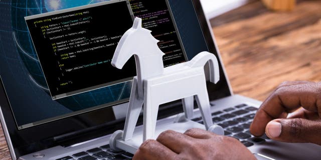 White mini Trojan horse model placed on the keyboard of a laptop with data on the screen