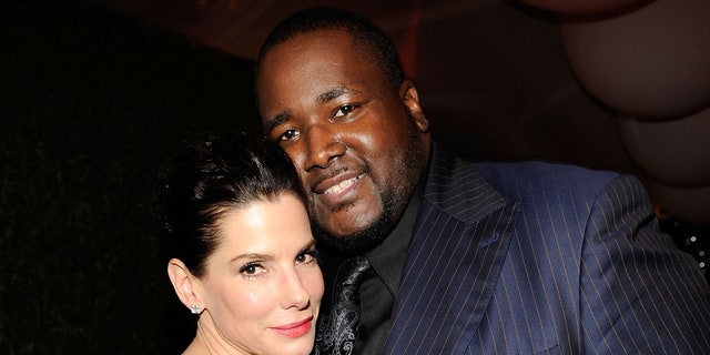 Sandra Bullock leans against Quinton Aaron in a blue pinstripe suit and black shirt and tie
