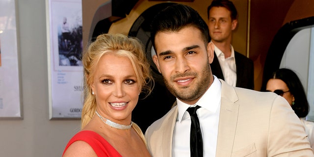 Britney Spears in a red dress and Sam Asghari in an off-white/tan suit and black tie
