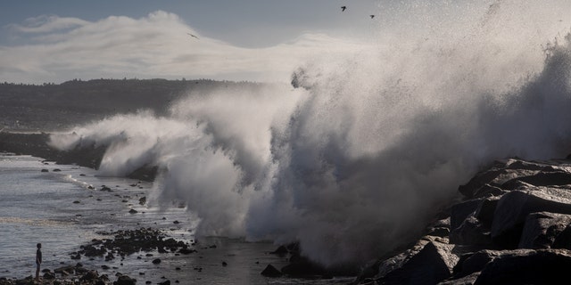 A boy plays in the water as giant waves crash over the breakwall of Redondo Beach