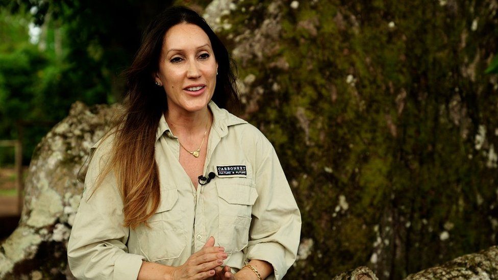 Janaína Dallan is CEO of Carbonext, which works on carbon capture projects. She is seen being interviewed in front of a tree and wearing a light shirt.