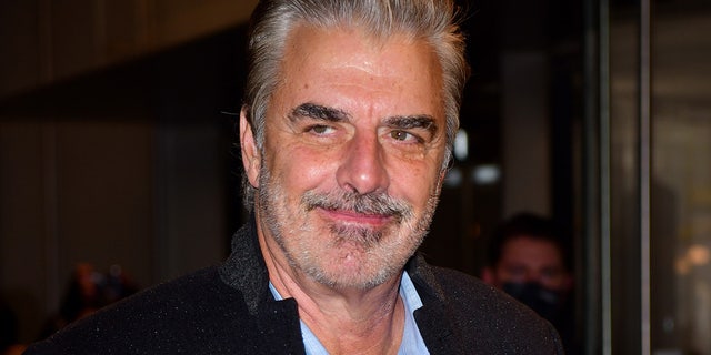 Chris Noth soft smiles and looks to his right while walking into the premiere of "And Just Like That..." wearing a blue shirt and black jacket