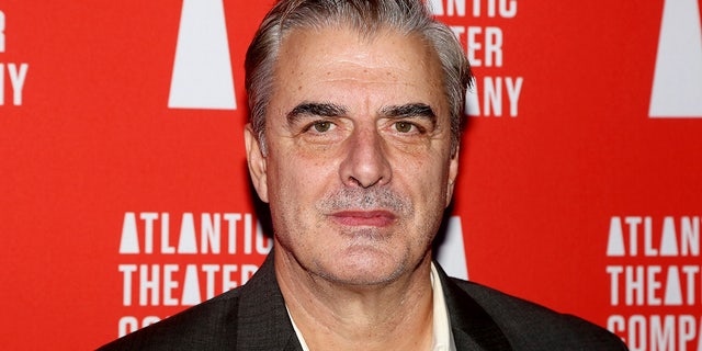 Chris Noth looks directly at the camera wearing a black suit and white shirt in New York City on a carpet