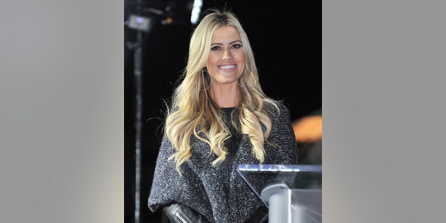 Christina Hall smiles at a podium in a dark grey sweater
