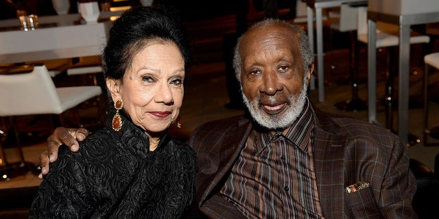 Jacqueline Avant soft smiles in a black outfit next to Clarence Avant in a brown jacket and printed shirt at a SAG-AFTRA Foundation Patron of the Artists Awards