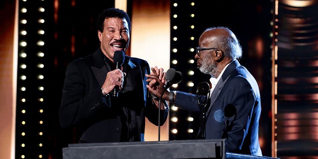 Lionel Richie holds a microphone as he presents Clarence Avant with an award at the Rock & Roll Hall of Fame induction