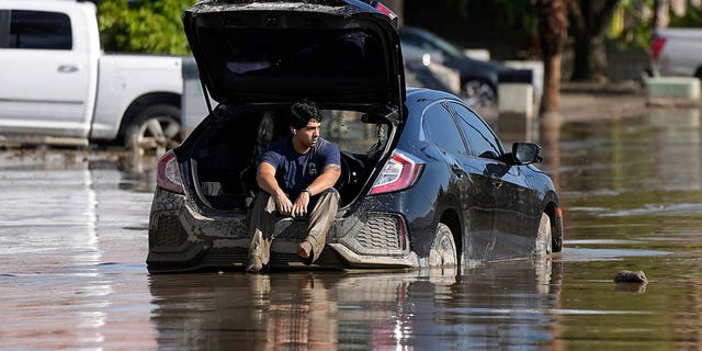 man waits in car stuck in flooded street
