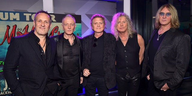Vivian Campbell, Phil Collen, Rick Allen, Rick Savage, and Joe Elliott all in black outfits pose for a photo at a press conference announcing their joint tour with Mötley Crüe