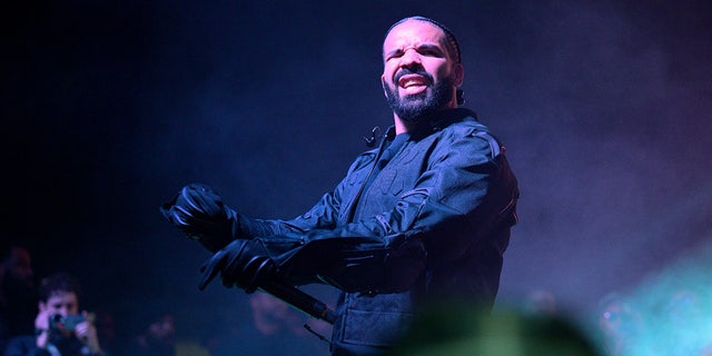 Drake in a black jacket and gloves performs on stage in Atlanta