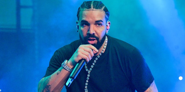Drake in a black shirt and long chain raps into a microphone while onstage in Atlanta