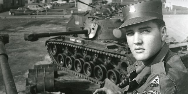Elvis Presley poses for portrait by military tanks