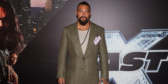 Jason Momoa in a green suit with a chain necklace on the carpet in Auckland, New Zealand