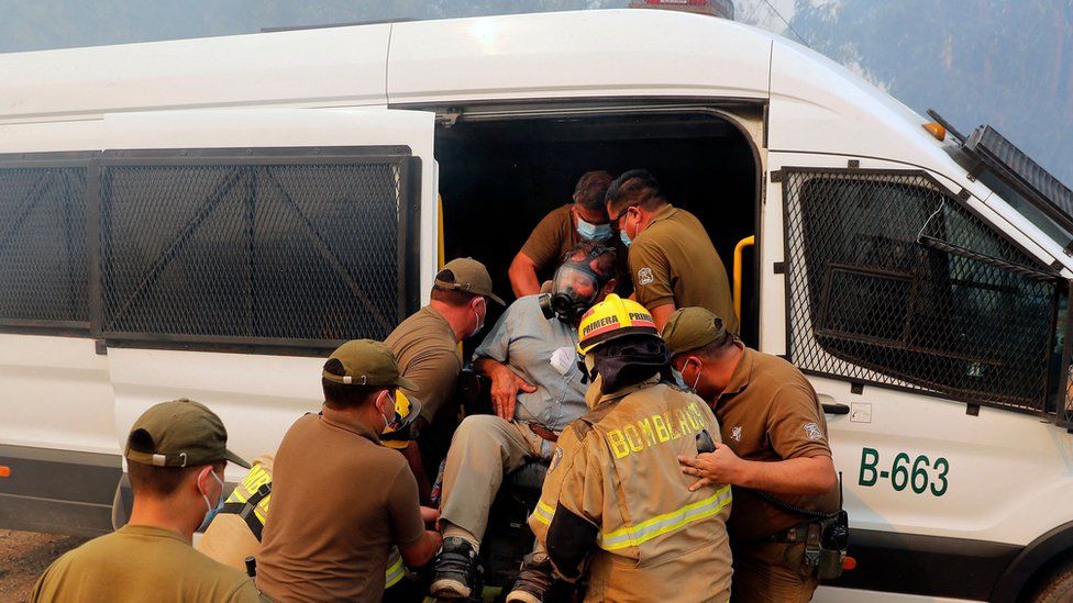 Firefighters and police evacuate a person in a wheelchair after a forest fire approached his house. in Ninhue, Ñuble Region, in Chile, on February 10, 2023. Forest fires raged for more than a week in south-central Chile, leaving at least 24 people dead.