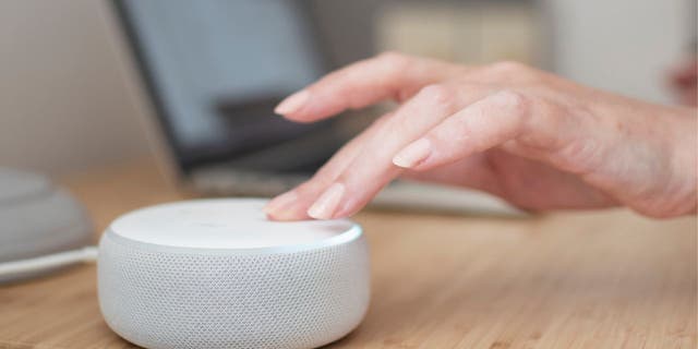 White Amazon Alexa device on a light wooden table with a hand touching the device