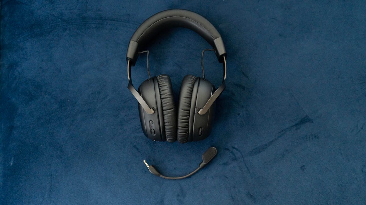 The HyperX Cloud 3 Wireless shown direct from above lying on a slate blue faux suede surface with the mic detached and curved beneath it