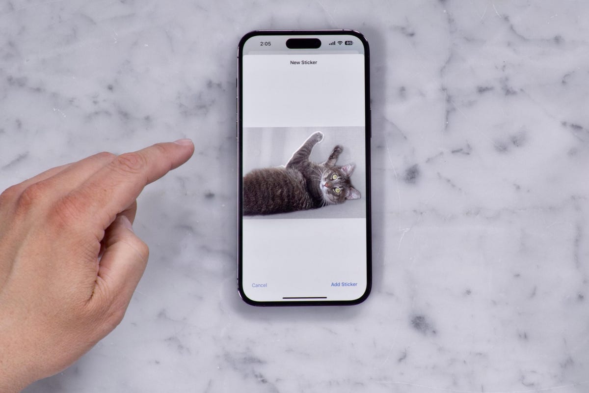 A hand making a custom sticker on an iPhone from a photo of a cat