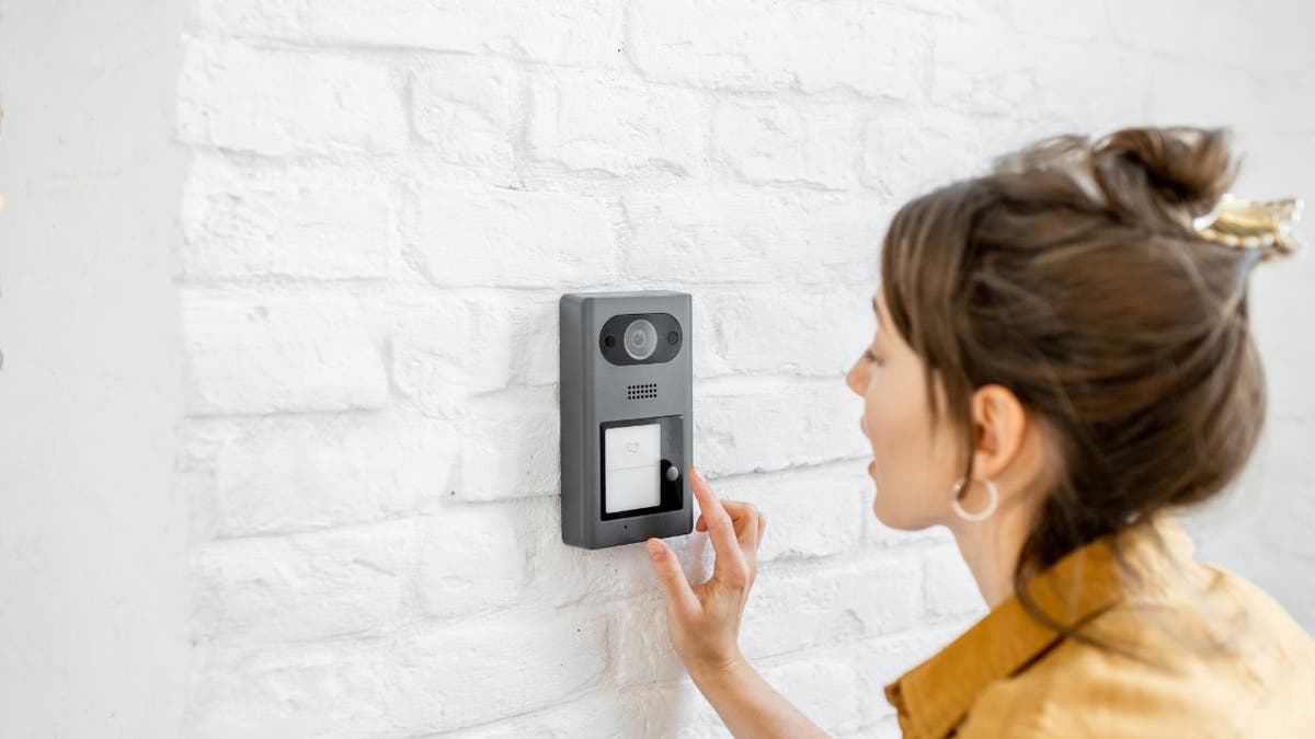 Photo of a woman pressing a button on a doorbell camera.