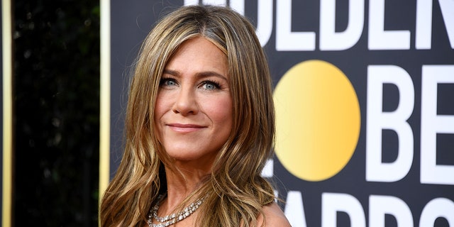 Jennifer Aniston soft smiles on the Golden Globes Carpet wearing a chain necklace