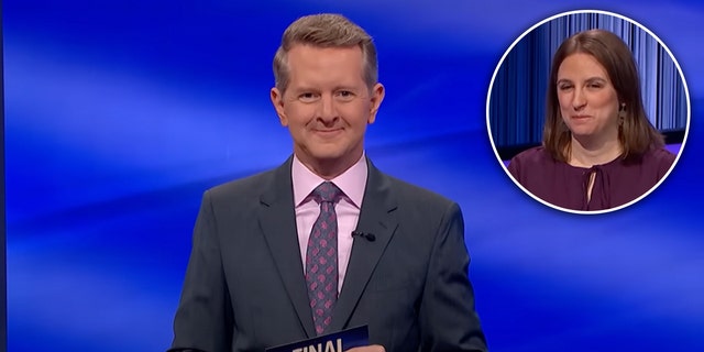 Ken Jennings holds a card on "Jeopardy" wearing a dark suit and a pink shirt with a purple tie