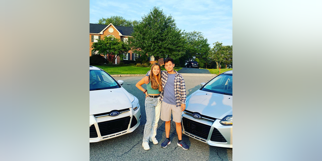 Hannah and Collin Gosselin pose for a picture in between two matching silver Ford cars
