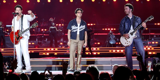 Nick in all white, Joe Jonas in a jersey and Kevin in a blue jacket perform at Yankee Stadium for opening night of "The Tour"