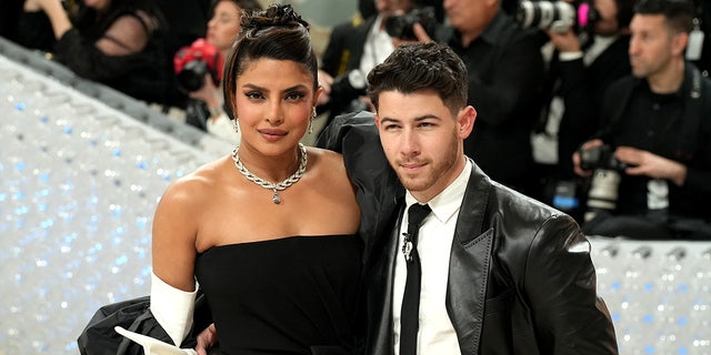 Priyanka Chopra in a black gown and updo smiles on the Met Gala carpet with husband Nick Jonas in a leather black suit