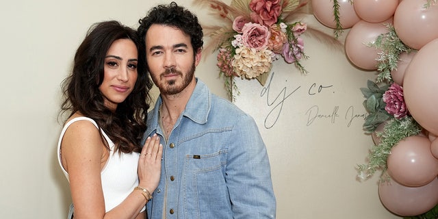 Danielle Jonas in a white tank top places her hand on her husband Kevin Jonas' chest, he's wearing a jean jacket at a boutique